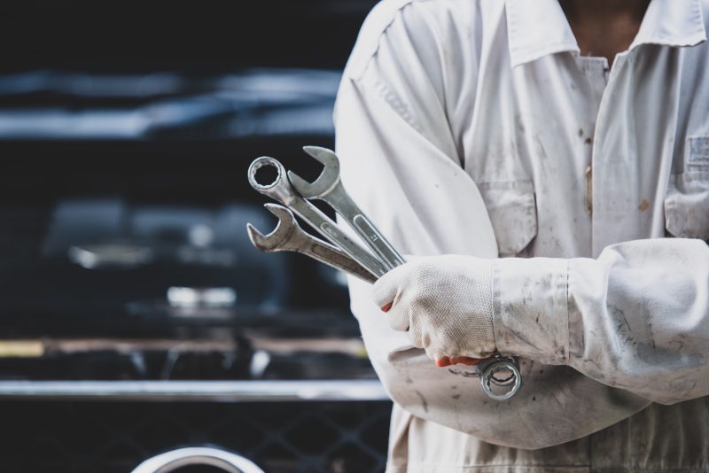 Car repairman wearing a white uniform standing and holding a wre